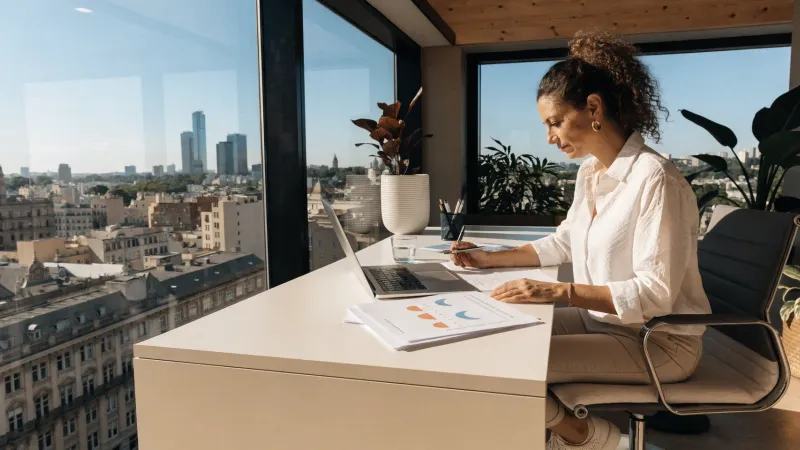 Profesional de BeeMyHost trabajando con documentos financieros y reportes de propiedades con vista a Buenos Aires